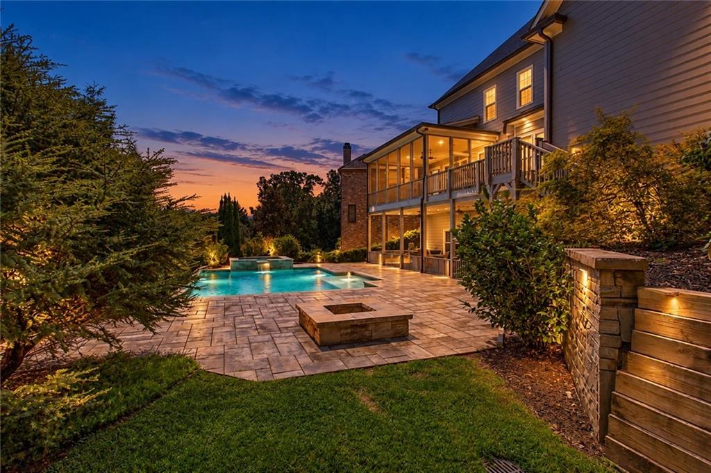 Backyard pool and stone patio beside a two-story home at dusk.