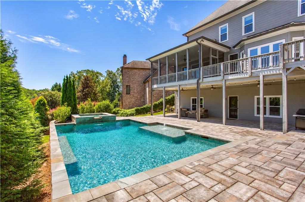 Backyard pool with raised spa beside a broad stone patio and covered porch.