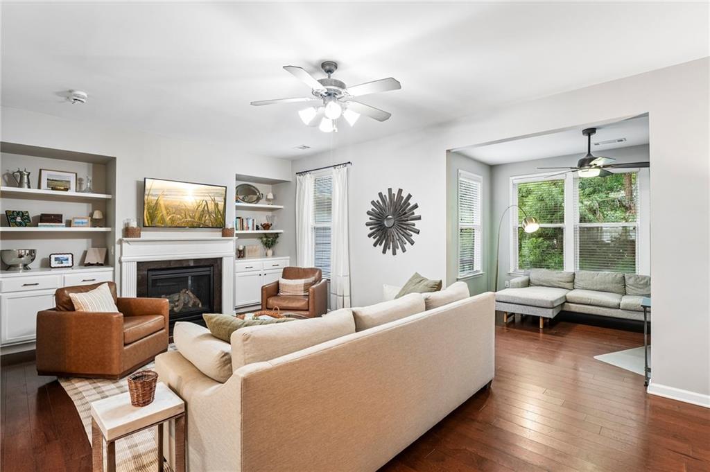 Living room with a white fireplace, built-in shelves, and a sectional facing a sunny window seating area.