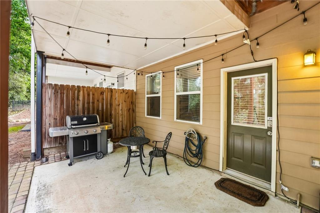 Covered patio with a barbecue grill, small table and chairs, and string lights.