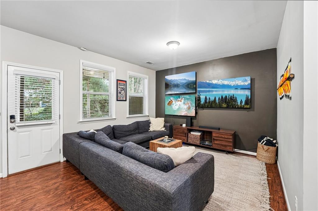 Living room with a dark gray sectional, landscape displays on a charcoal accent wall, and hardwood floors.