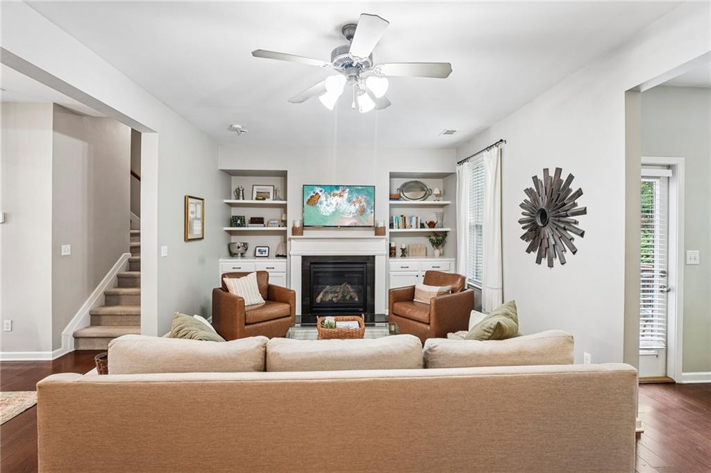 Living room with a fireplace, built-in shelves, and brown leather armchairs facing a beige sofa.