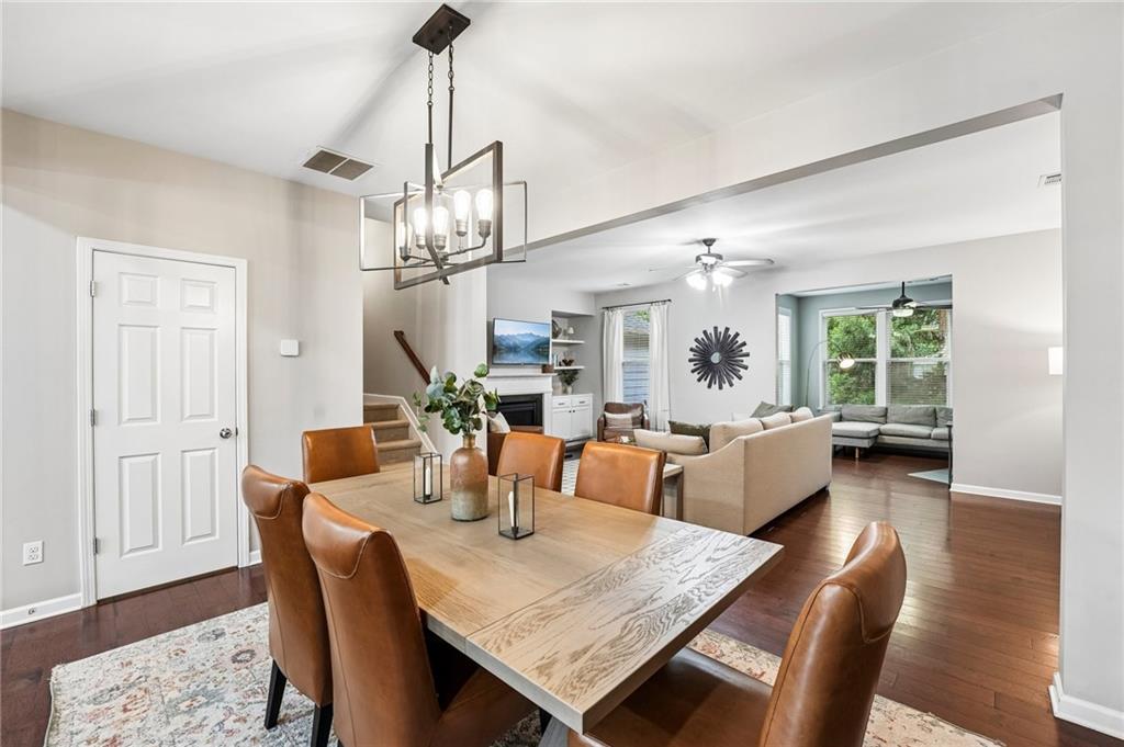 Open-plan dining and living room with a wood table, leather chairs, fireplace, and bright windowed sitting area.