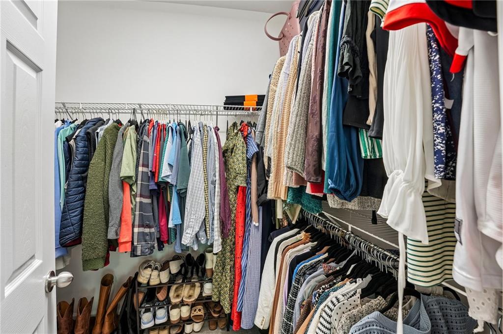Walk-in closet with clothes on both sides and shoes arranged on racks.