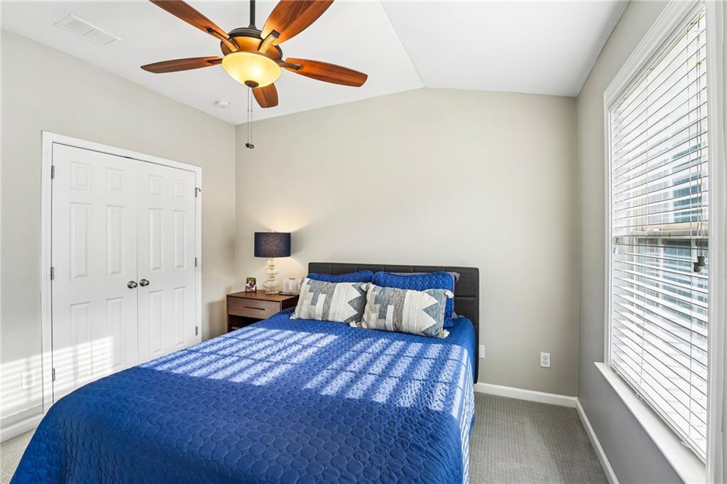 Bedroom with a blue quilted bed, white double closet doors, and a large window with blinds.