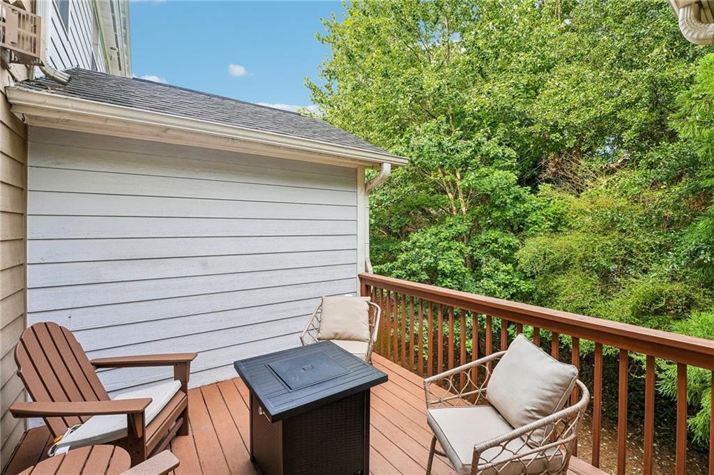 Wooden deck with Adirondack chairs and a black fire table overlooking leafy trees.