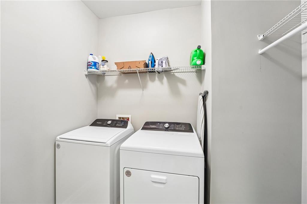 Laundry room with a white washer and dryer beneath wire shelves stocked with supplies.