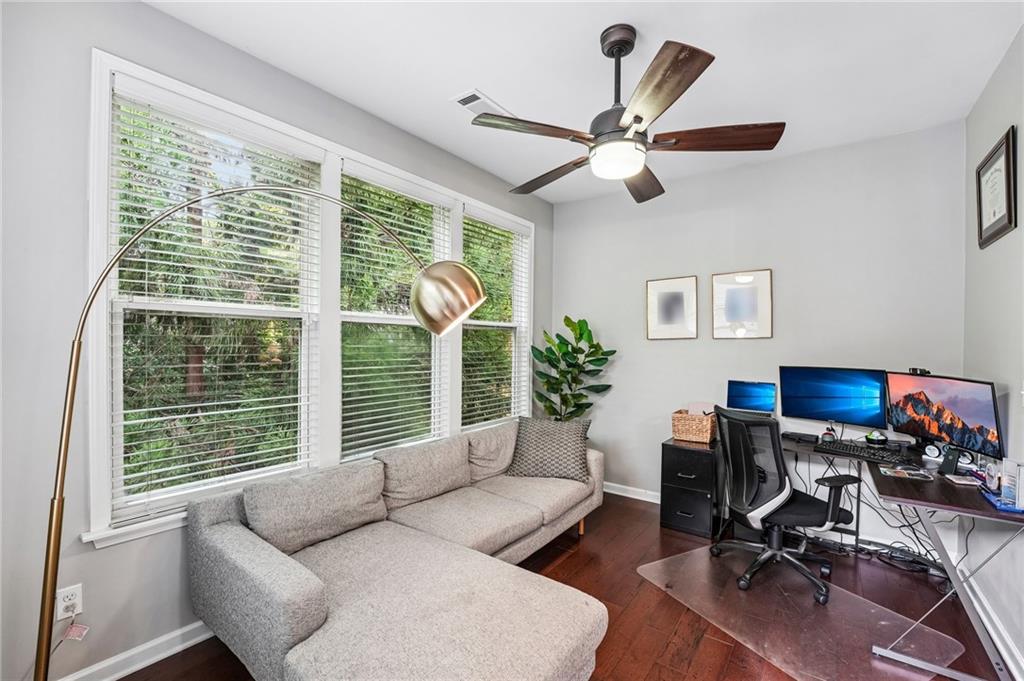 Furnished home office with a gray sectional sofa, wide windows, and a multi-monitor desk setup.
