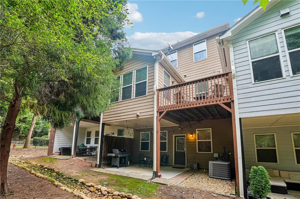 Townhouse rear with a raised wooden deck, covered patio, grill, and mature trees.