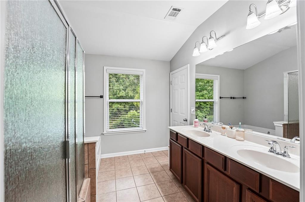 Bathroom with a double-sink vanity, large mirror, and textured glass shower.