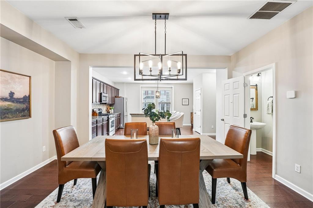 Dining room with a large table, brown leather chairs, and a geometric chandelier beside an open kitchen.