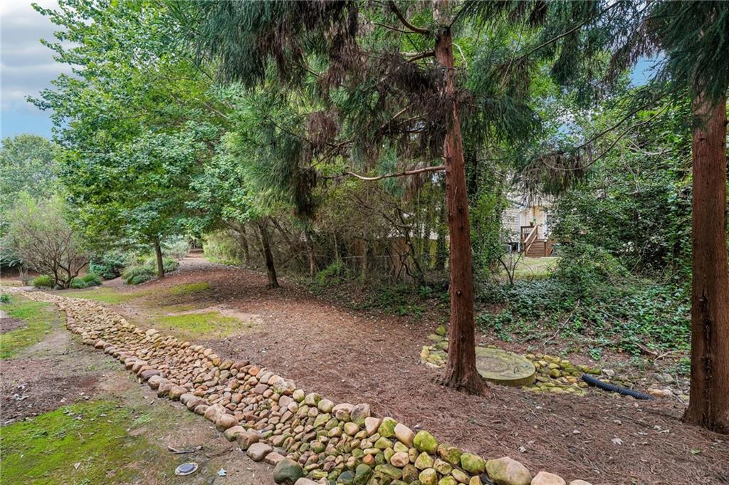 Wooded yard with mature trees and a curved stone border along a mulched path.
