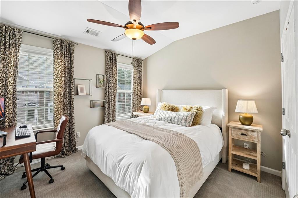 Staged bedroom with a white bed, patterned curtains, and a desk beside two windows.