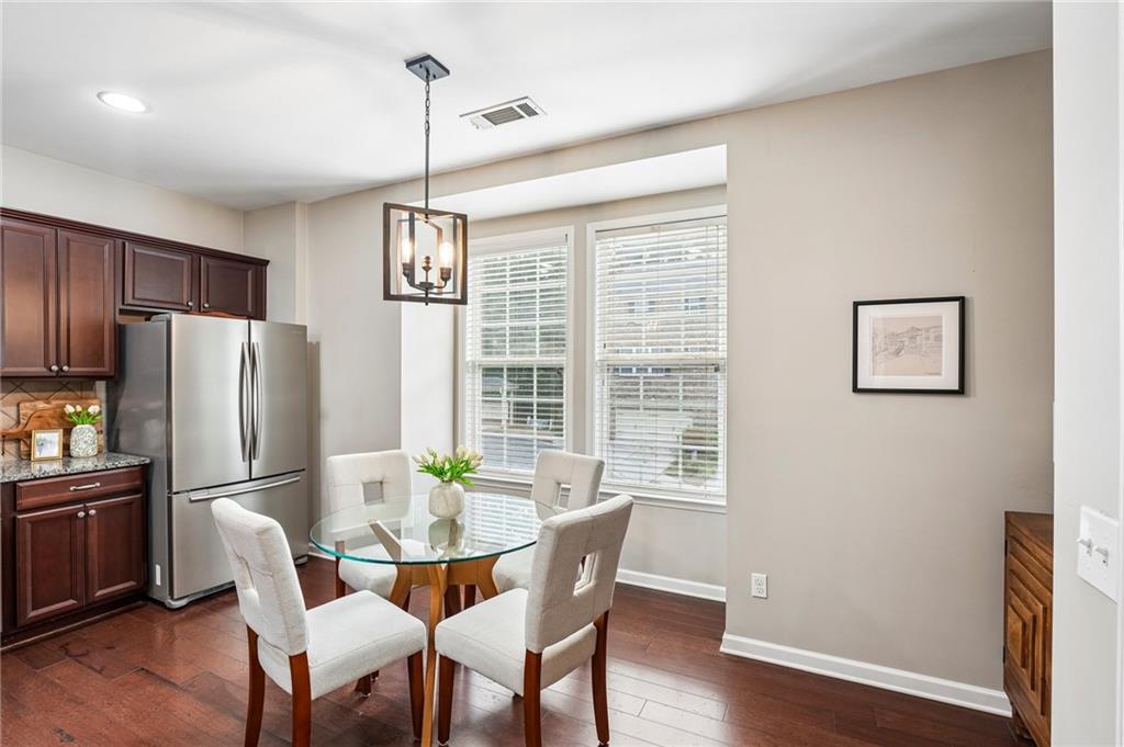 Dining area with a round glass table and four upholstered chairs beside dark kitchen cabinetry.