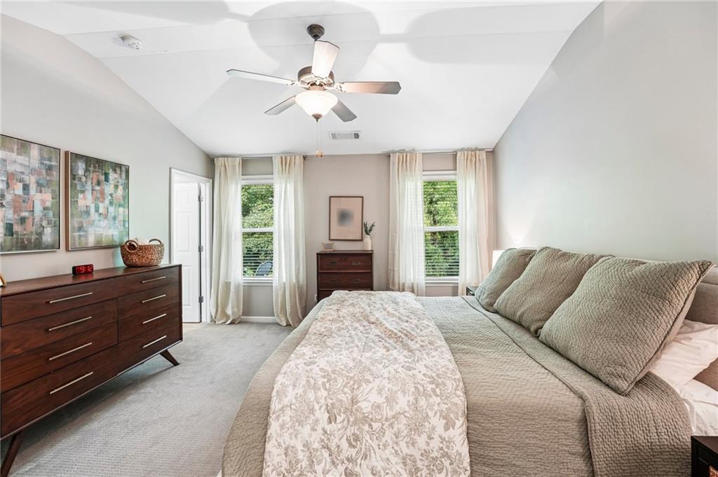 Bedroom with a large neutral-toned bed, tall curtained windows, and dark wood dresser.