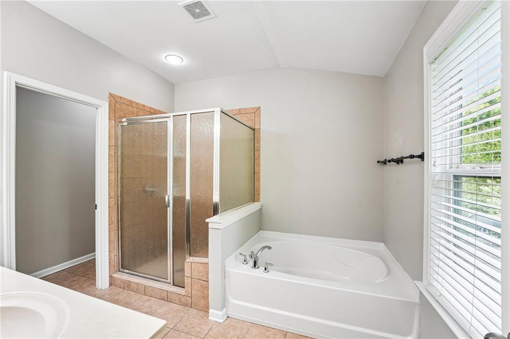 Bathroom with a white soaking tub, separate glass shower, and large window with blinds.