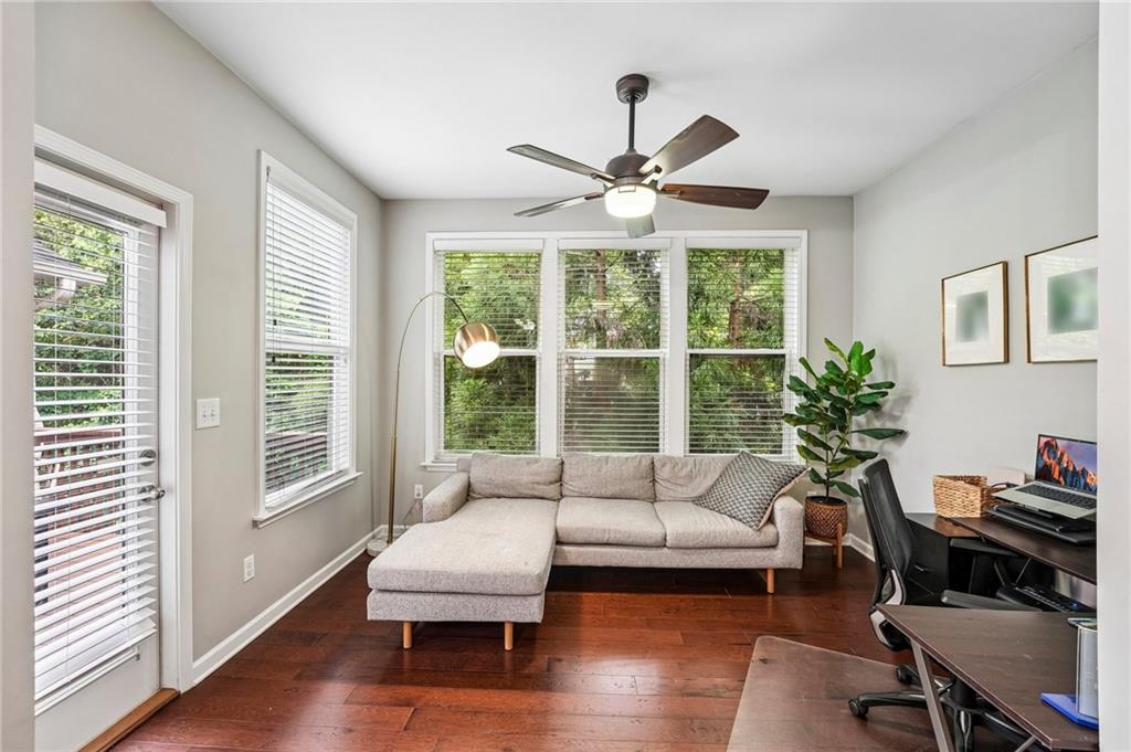 Living room with a gray sectional, hardwood floors, and wide windows overlooking leafy trees.