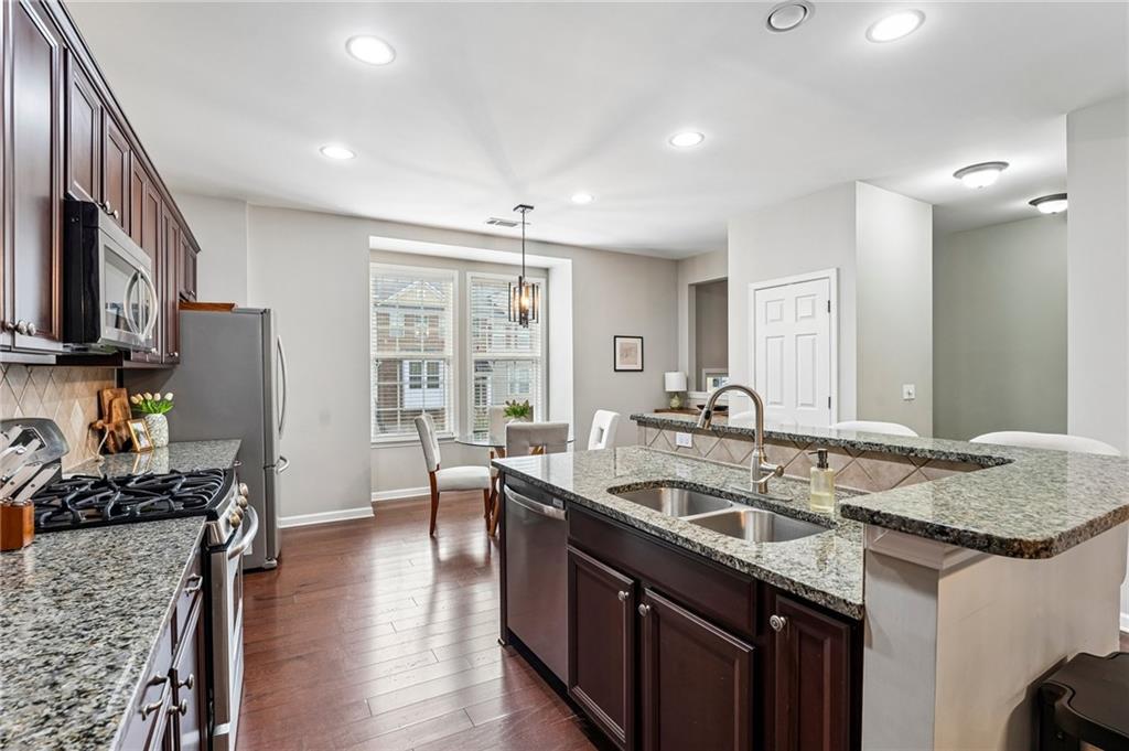 Kitchen with a granite island and double sink, dark cabinetry, stainless steel appliances, and hardwood floors.