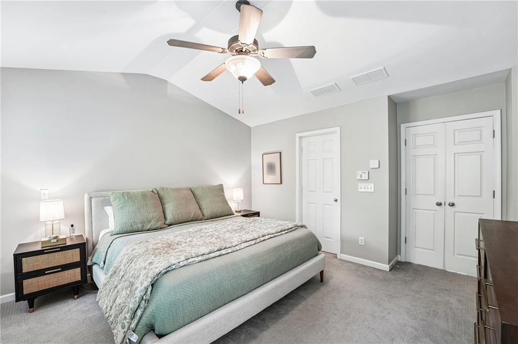 Furnished bedroom with a large muted-green bed, ceiling fan, and white double closet doors.