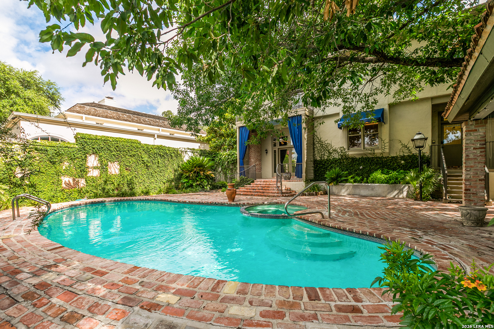 Backyard pool with a brick patio, mature trees, and outdoor entertaining space behind the home.