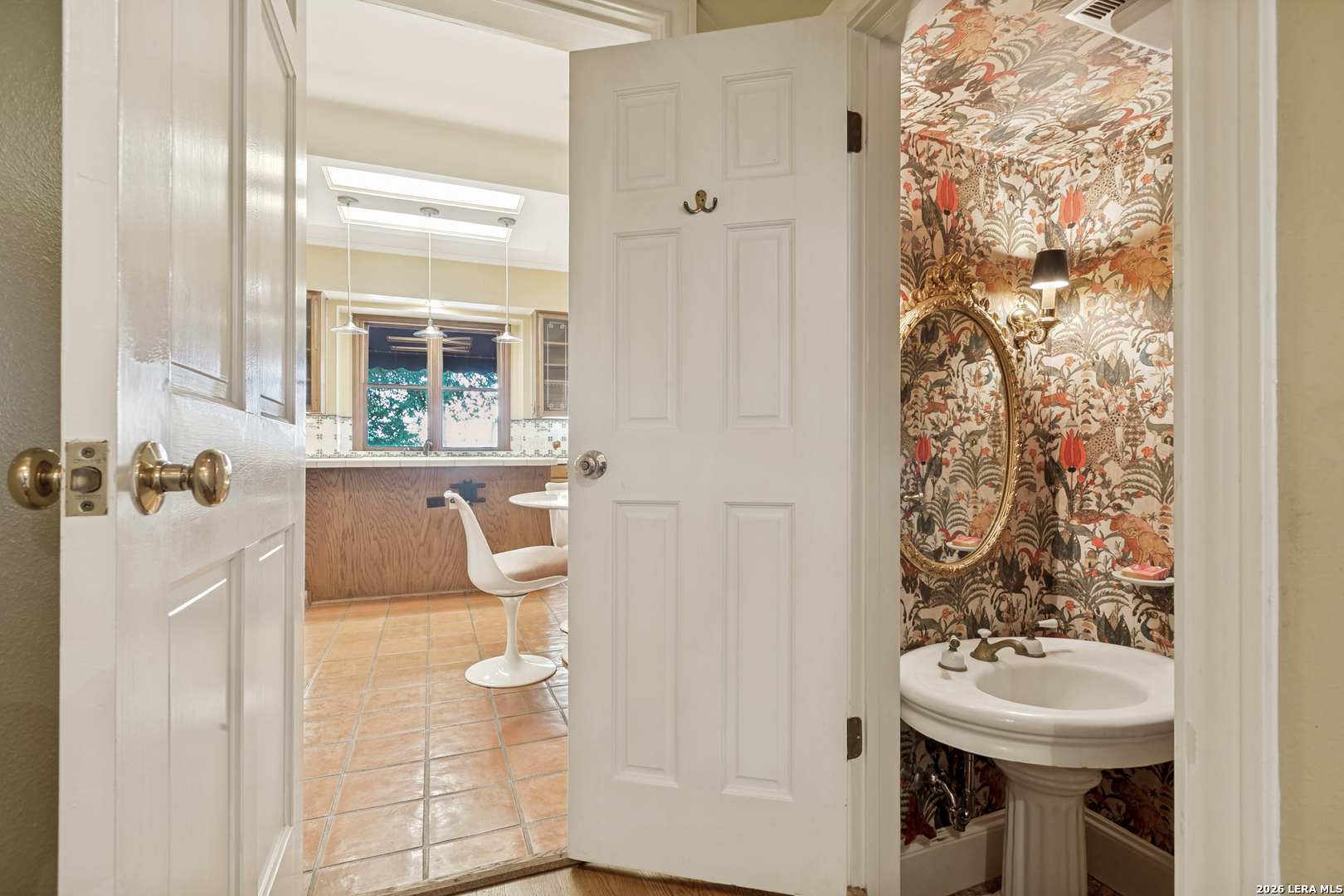 Powder bath with patterned wallpaper, a pedestal sink, and an ornate mirror near the kitchen.
