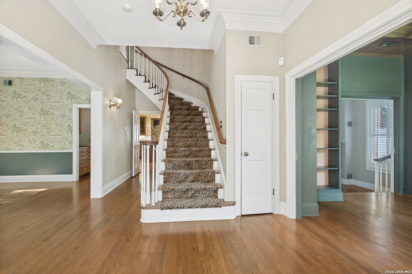 Grand entry hall with a curved staircase, hardwood floors, and views into the library and dining room.