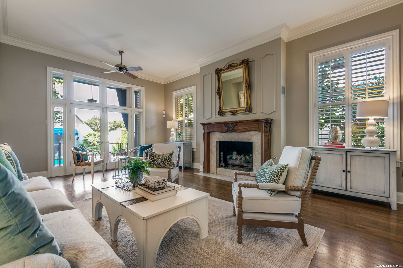 Elegant living room in a Terrell Hills home featuring a fireplace, hardwood floors, and French doors with pool views.