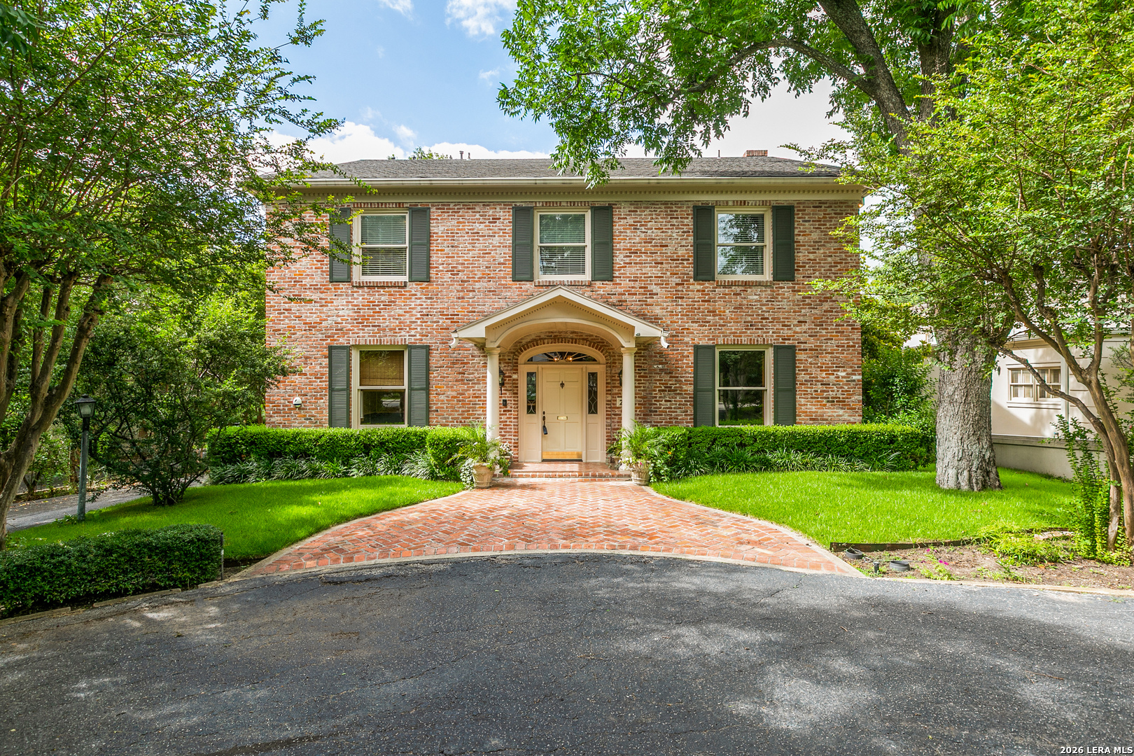 Traditional brick Terrell Hills home with manicured landscaping, mature oak trees, and a welcoming front entrance.
