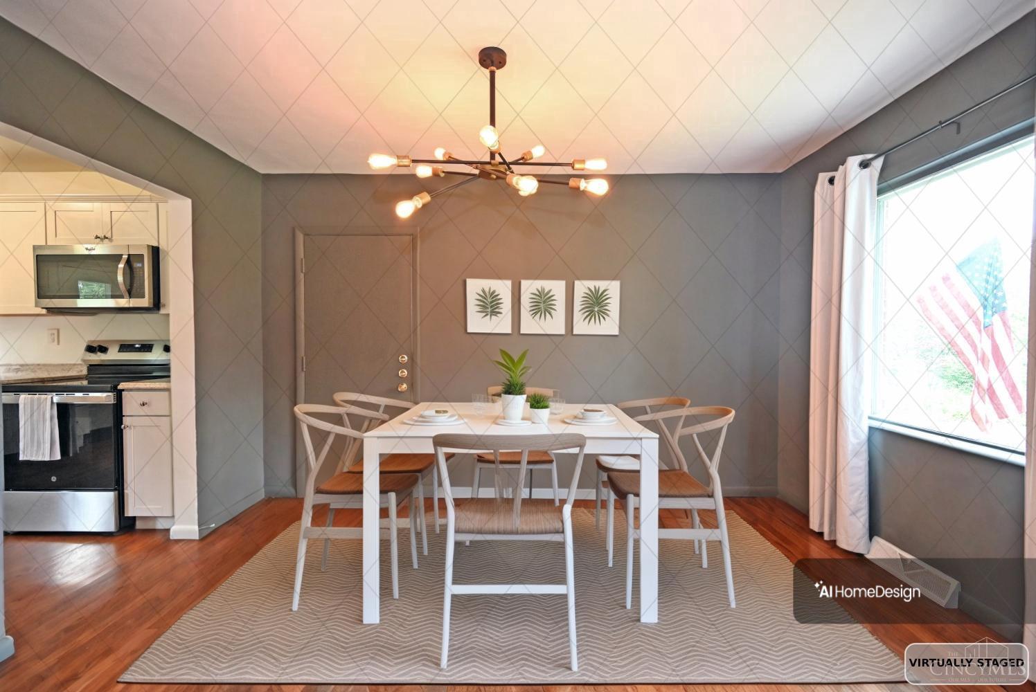 Dining area with a white table, branching chandelier, gray walls, hardwood floors, and a large window.