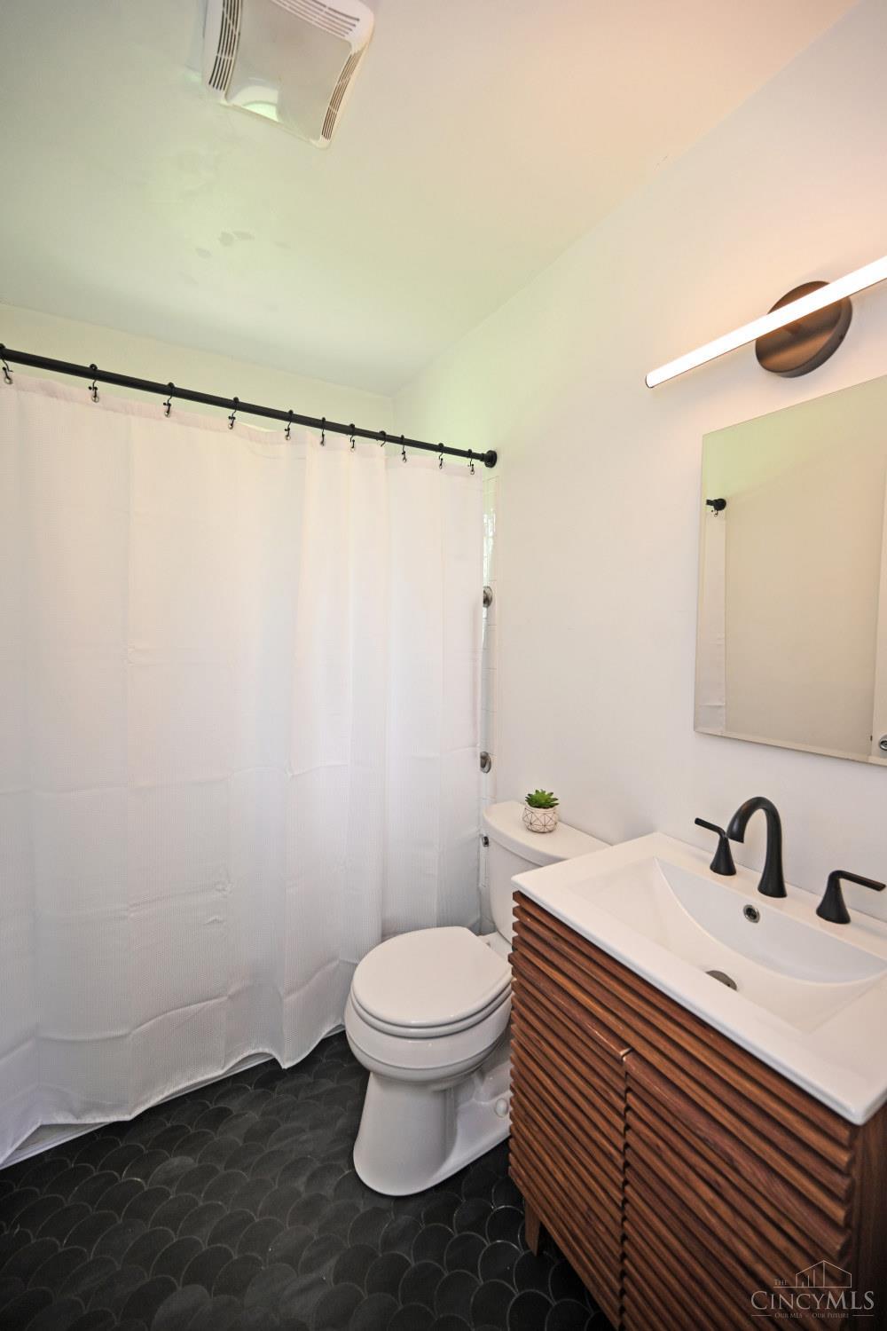 Bathroom with a wood-slat vanity, double sink, shower curtain, and dark scallop-pattern tile floor.