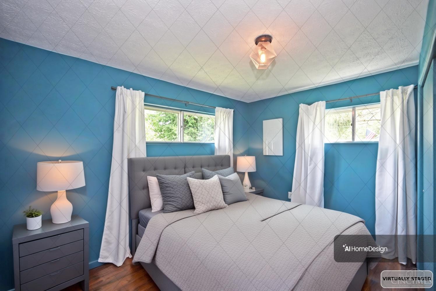 Bedroom with blue walls, a gray bed, light bedding, and two curtained windows.