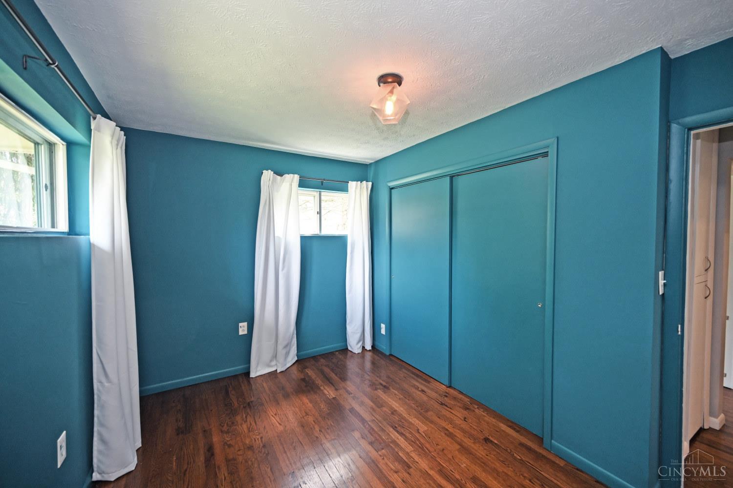 Empty bedroom with teal walls, dark hardwood floors, and a large sliding-door closet.