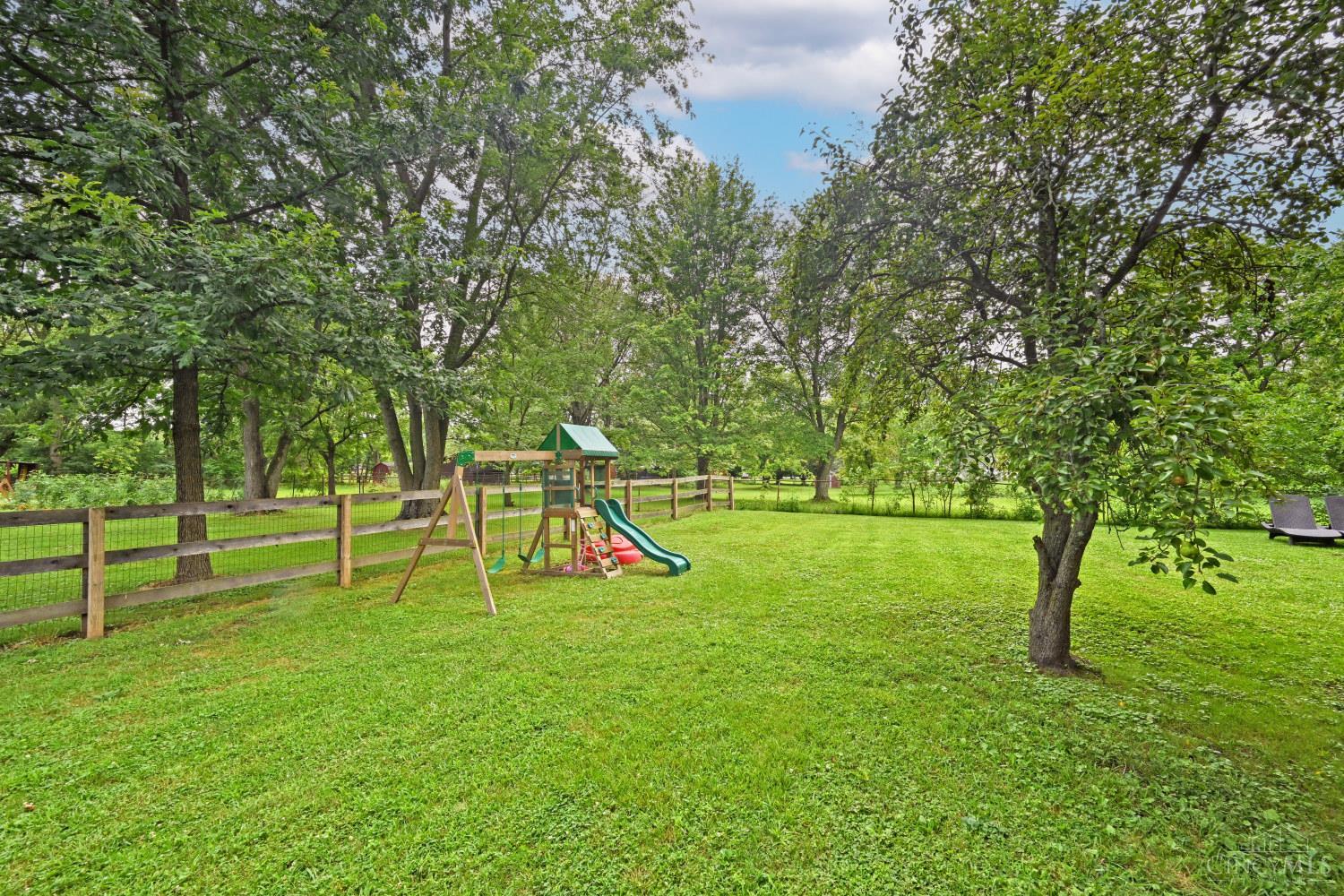 Tree-lined backyard with a fenced lawn and children’s playset with swings and slides.