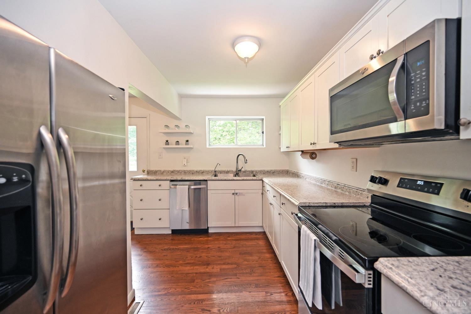 Kitchen with white cabinets, stainless steel appliances, stone counters, and dark hardwood floors.