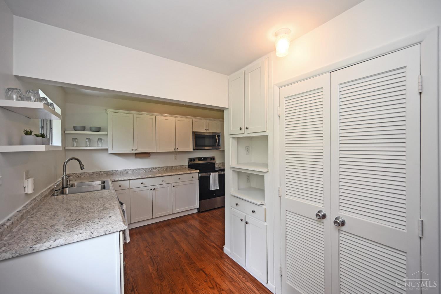 Kitchen with white cabinetry, granite counters, dark wood floors, and louvered pantry doors.