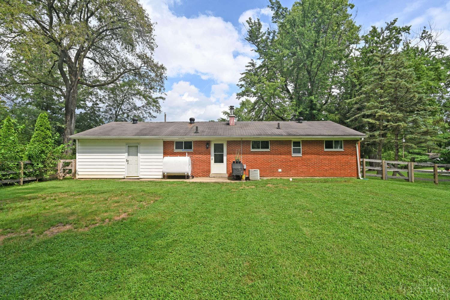 Single-story brick-and-siding home viewed from the rear, with a broad lawn and mature trees.