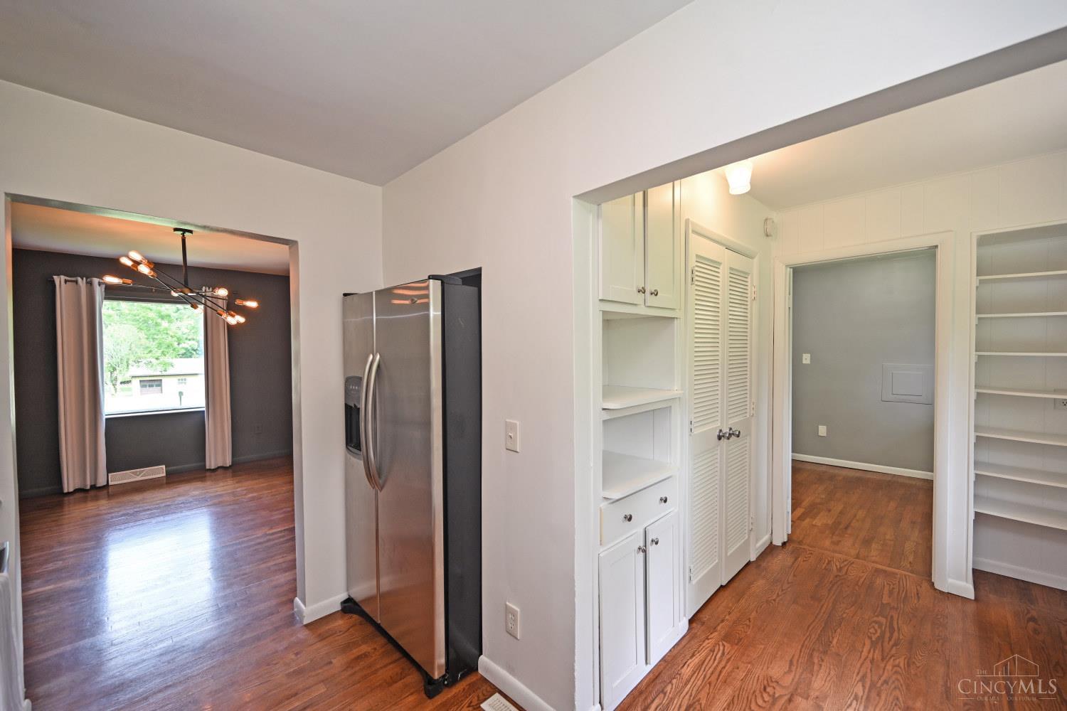 Kitchen with stainless steel refrigerator, white built-ins, and hardwood floors opening to a dining room.