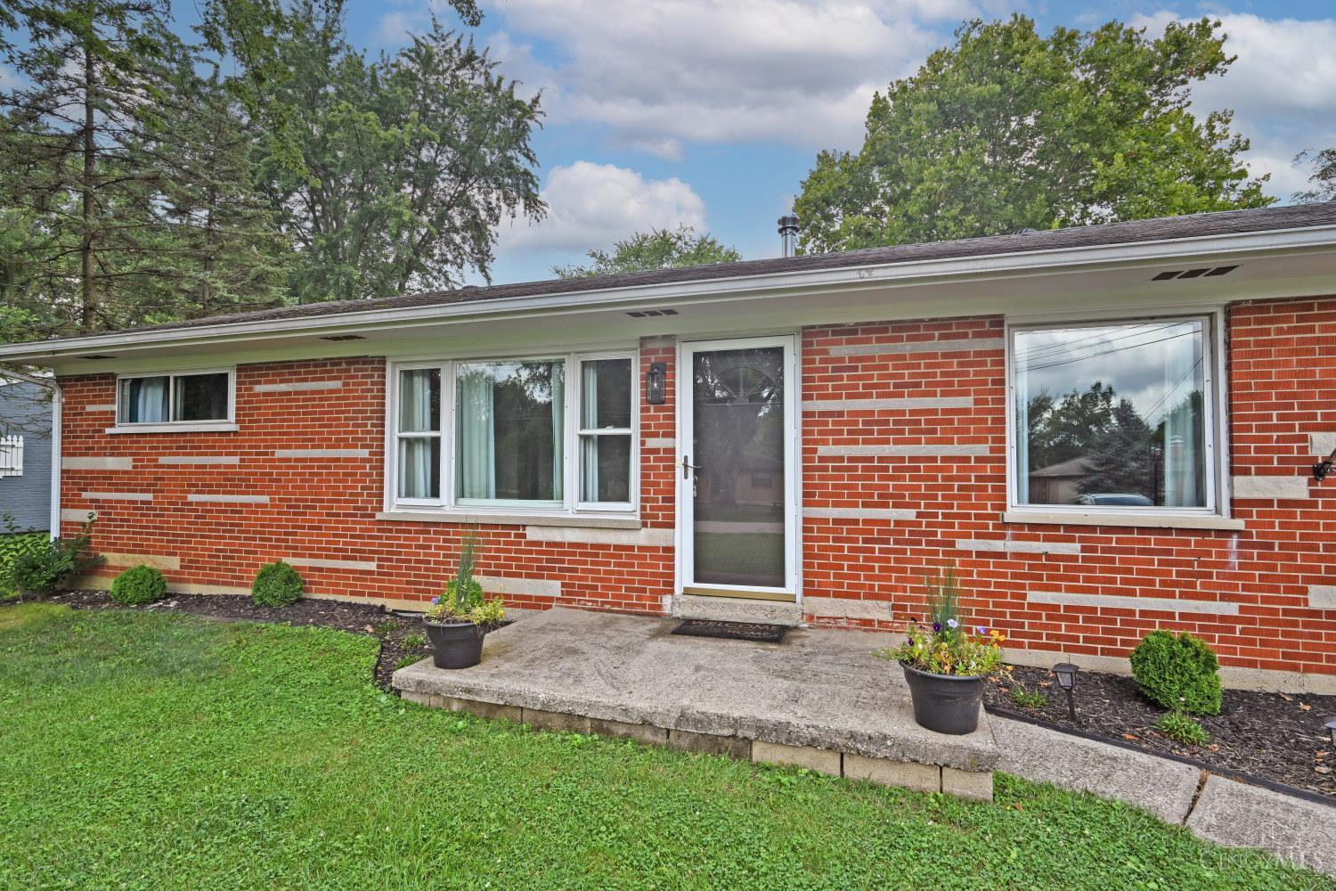 Single-story brick home with a screened entry, concrete patio, and potted flowers.