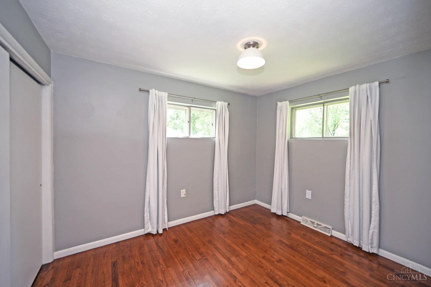 Vacant bedroom with hardwood floors, gray walls, and two curtained windows.