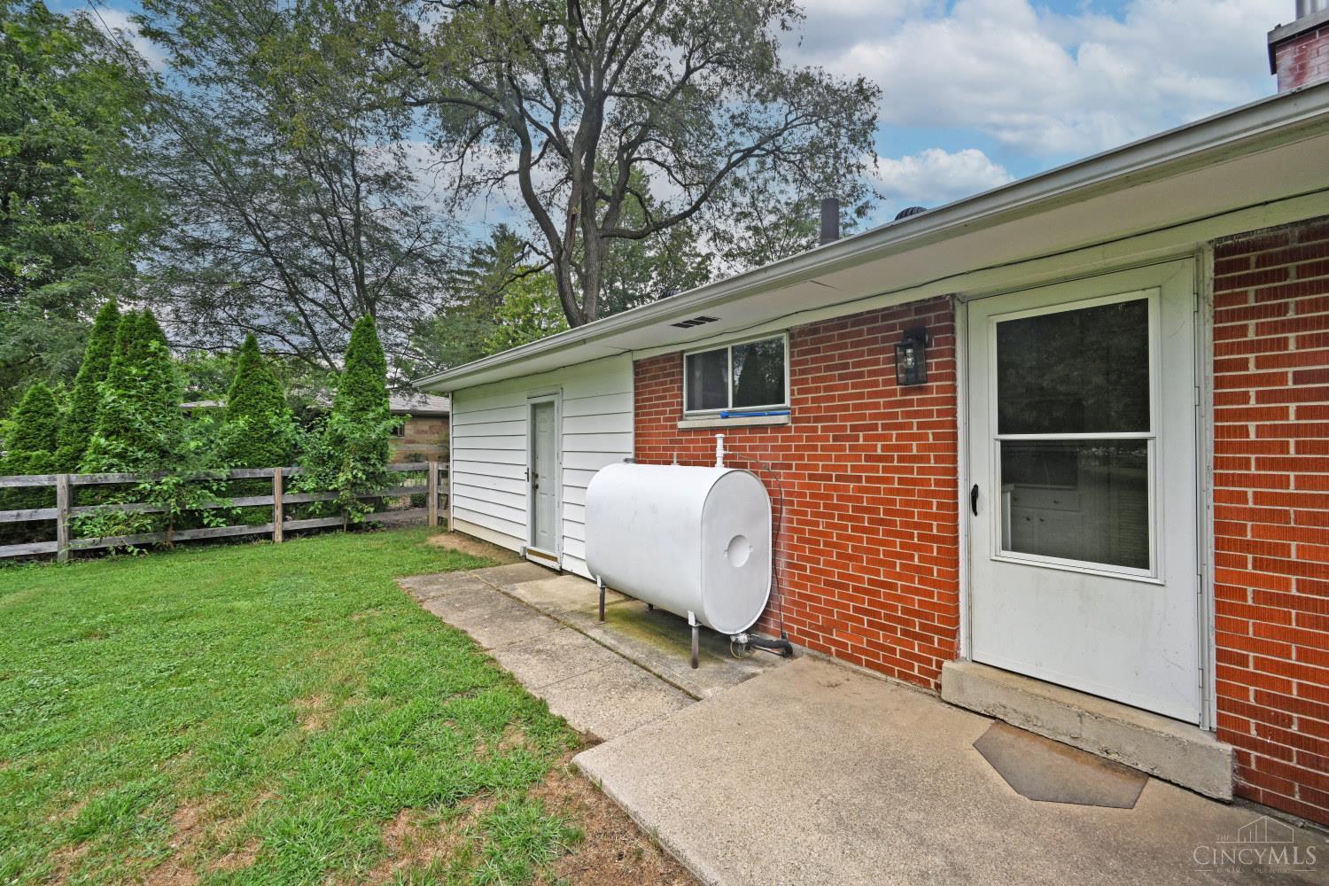 Brick home’s side entrance and patio beside a white tank, lawn, and fenced yard.