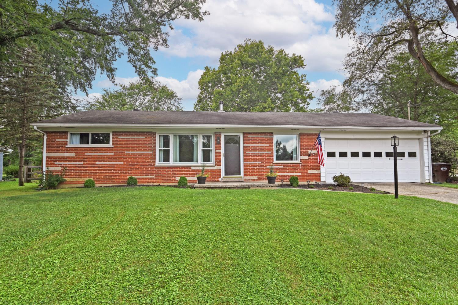 Red brick ranch home with an attached white garage, broad lawn, and mature trees.
