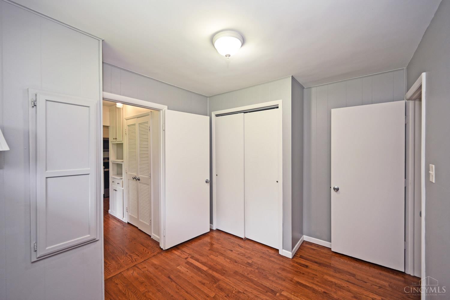 Empty bedroom with reddish hardwood floors and doors opening to a built-in dressing area.