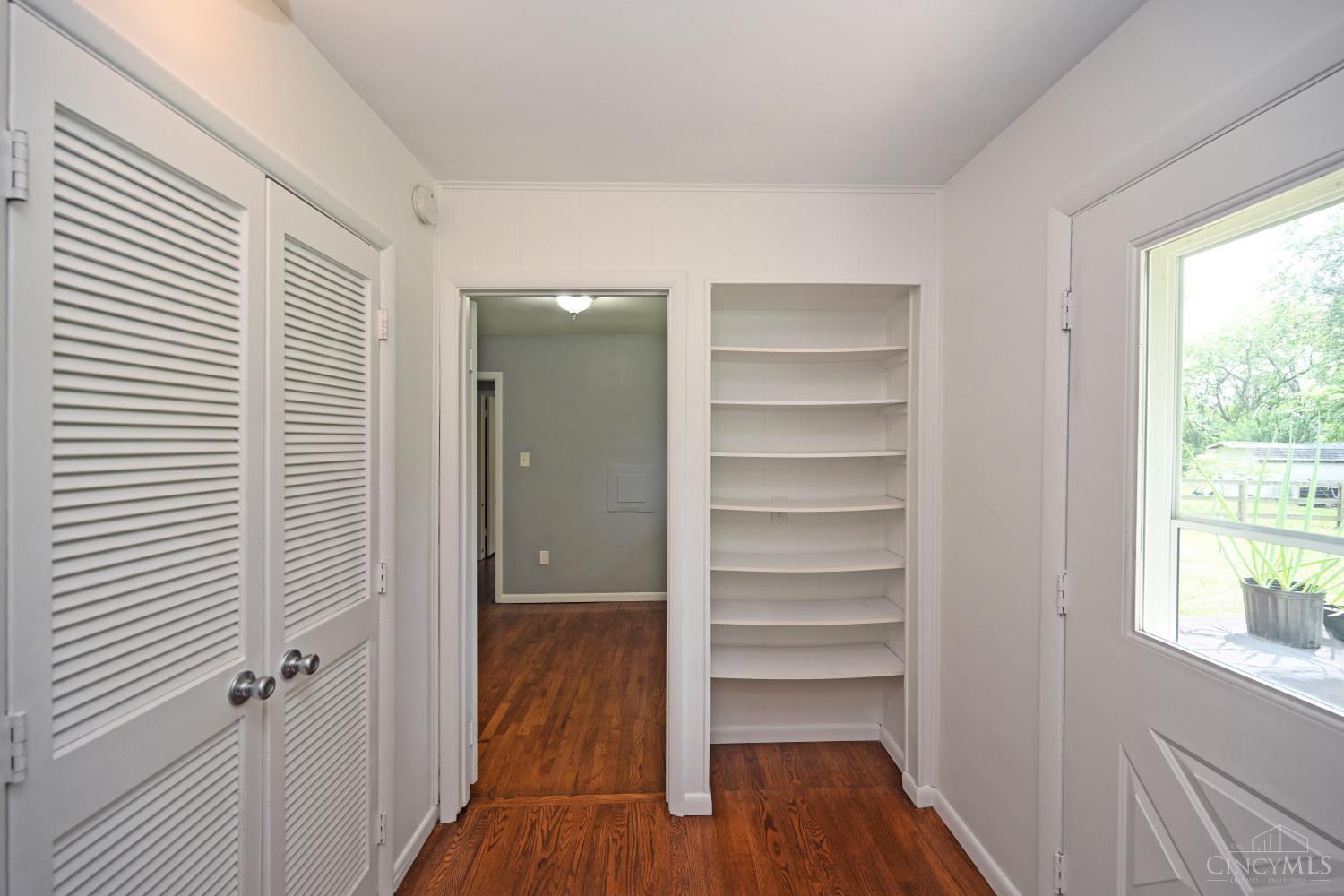 Bright room with wood floors, louvered closet doors, built-in shelves, and a window beside the exterior door.