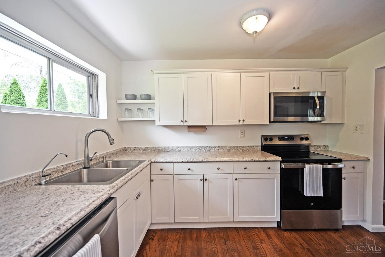 Kitchen with white cabinets, granite counters, stainless steel appliances, and a sink beneath a wide window.
