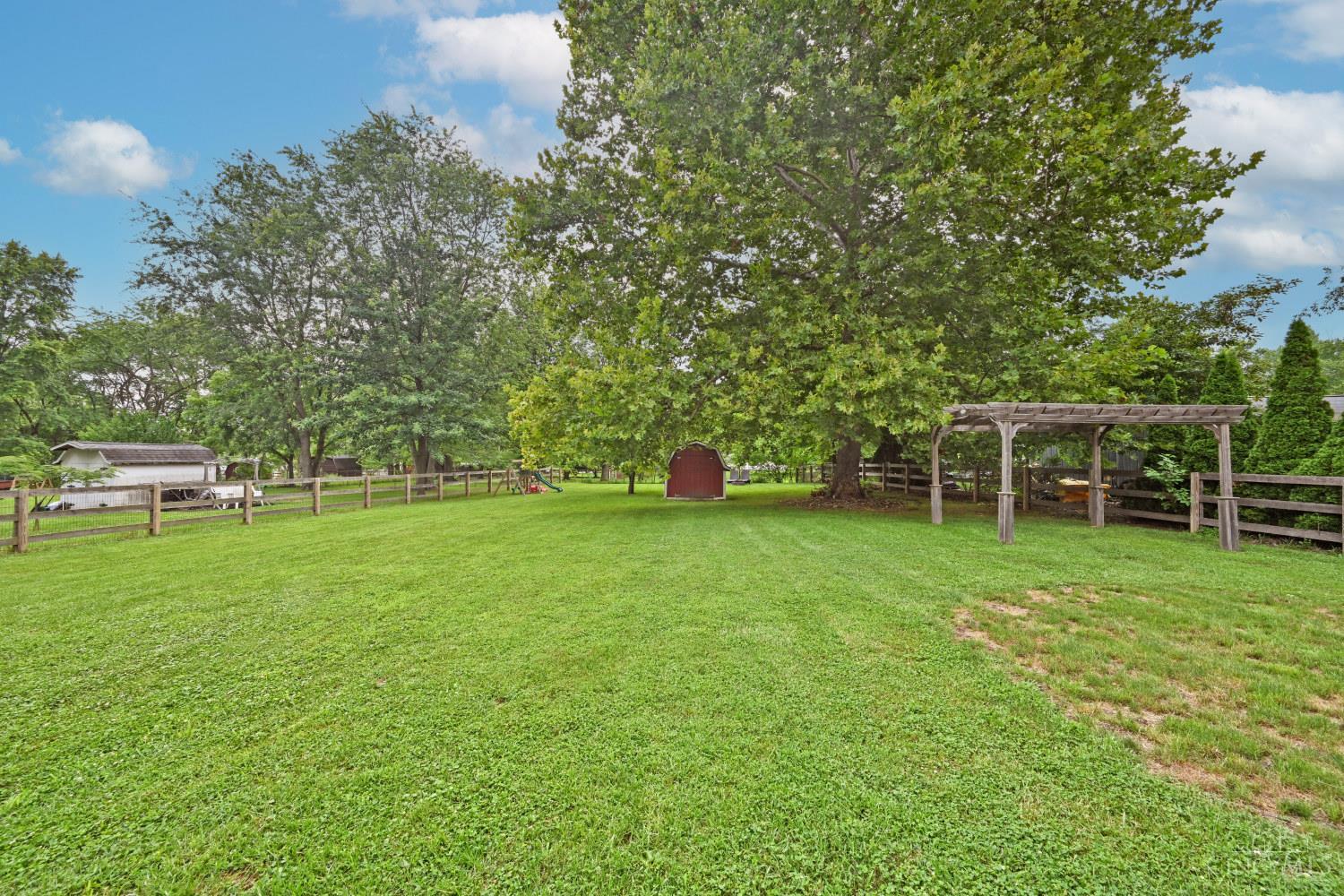 Fenced backyard with a broad lawn, mature trees, a red shed, and a wooden pergola.