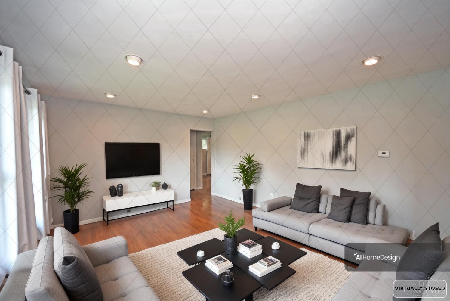 Living room with gray sofas, hardwood floors, a wall-mounted television, and a black coffee table.
