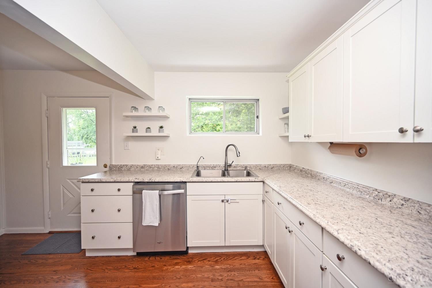 Kitchen with white cabinets, granite countertops, a double-basin sink, and warm hardwood floors.
