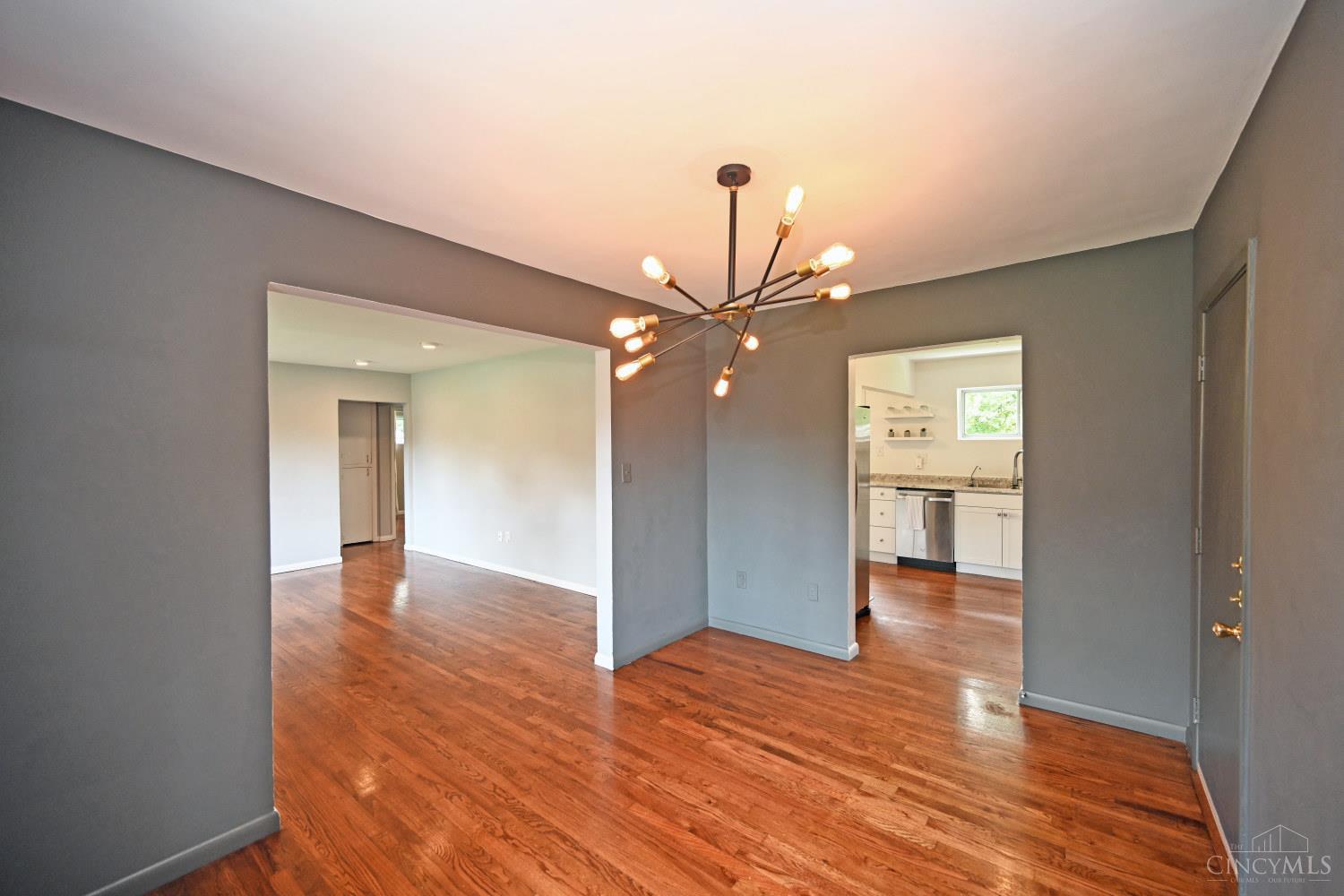 Dining area with polished hardwood floors, gray walls, and a branching chandelier overlooking the kitchen.