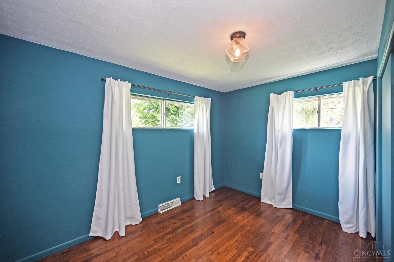 Empty room with teal walls, two curtained windows, and dark hardwood floors.