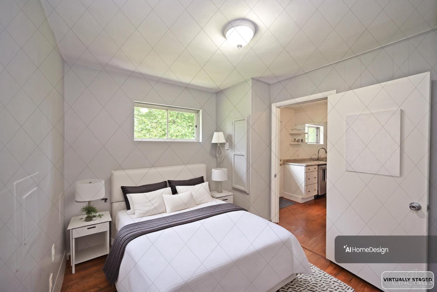 Virtually staged bedroom with a white bed, hardwood flooring, and doorway to an adjoining room.